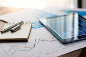 Tablet resting on financial graphs with a notepad and pen, representing business budgeting, data analysis, and valuation preparation